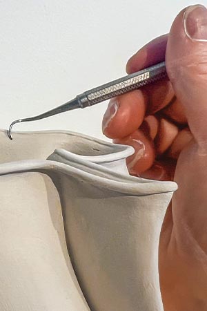 Image of a hand using a dental tool to carve a sculpture out of clay