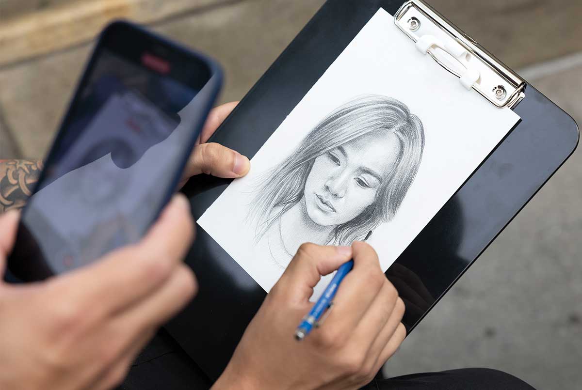 Image of a person creating a sketch from reference photo on their phone